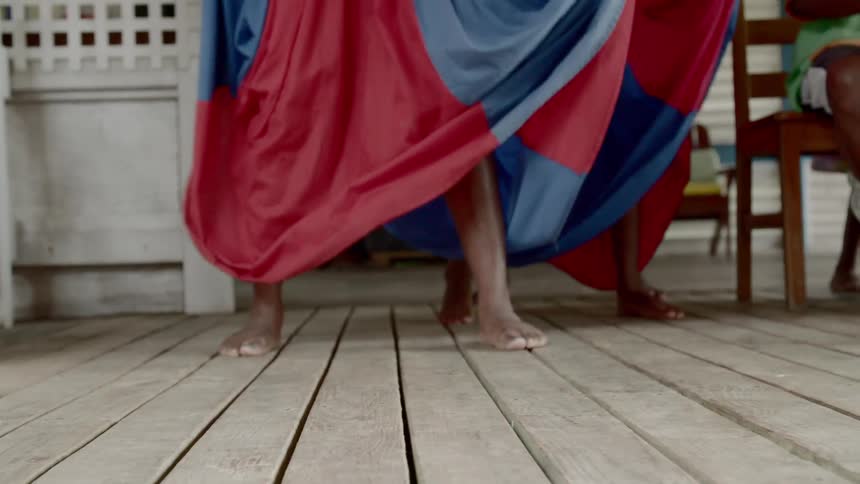 Women wearing wide colorful skirts dance barefoot on a a deck