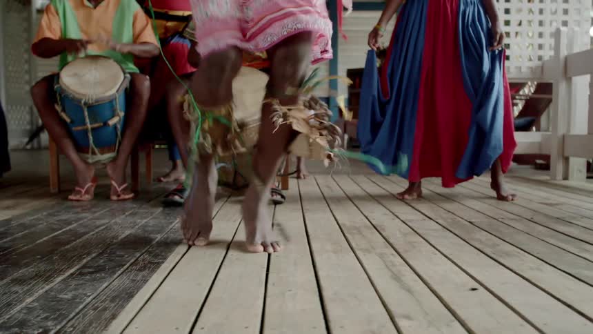 Boys play the drums while a girl dances barefoot on the porch