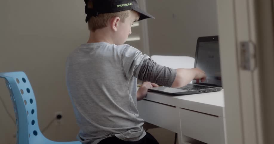 Boy sitting at desk uses laptop in bedroom