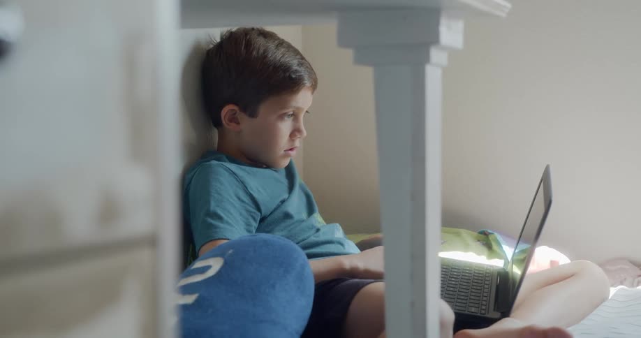 A young boy sits in a corner playing with a laptop on the floor