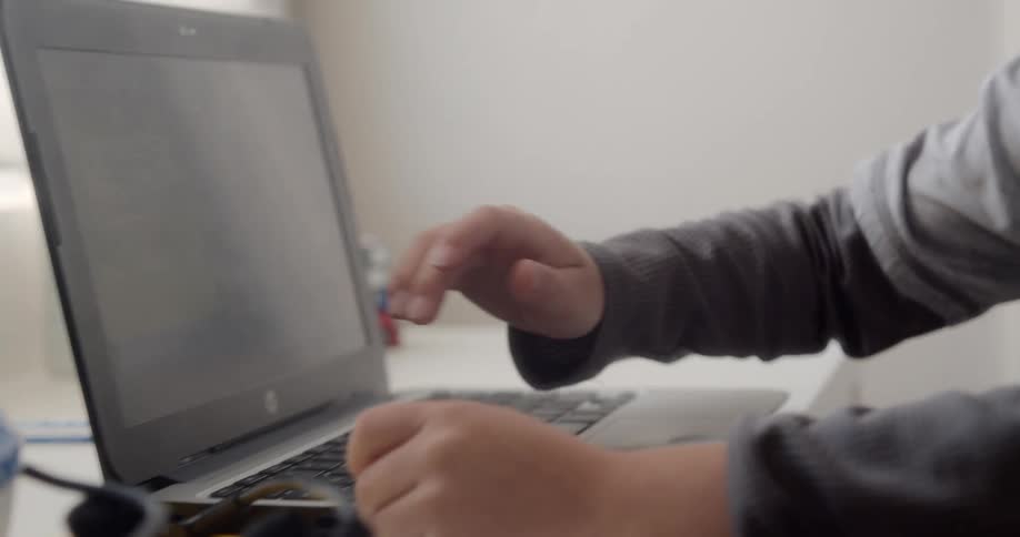 A boy typing on a laptop on a desk