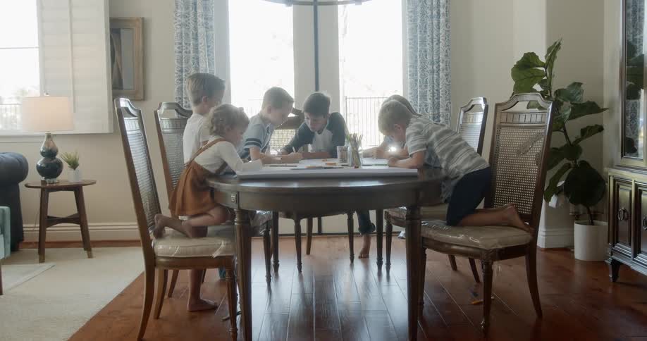 A group of friends sit at a dining table in a house drawing on paper