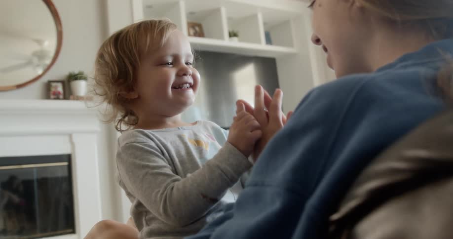 A teenager sits with a toddler on her knee and they clap hands together