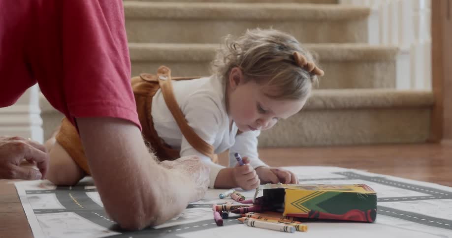A female child draws on a piece of paper with a crayon while crouching on the floor