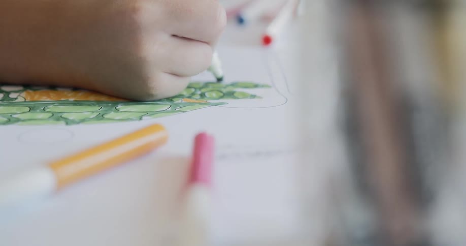 Kid drawing with markers on paper over table