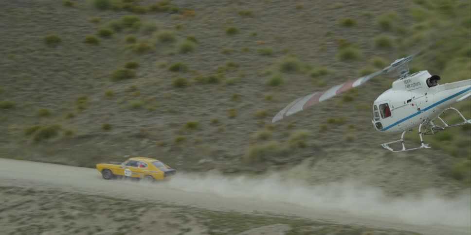 A white helicopter chasing after a yellow car on a dirt road