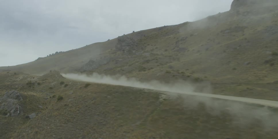A car races down a dirt road through desert hills