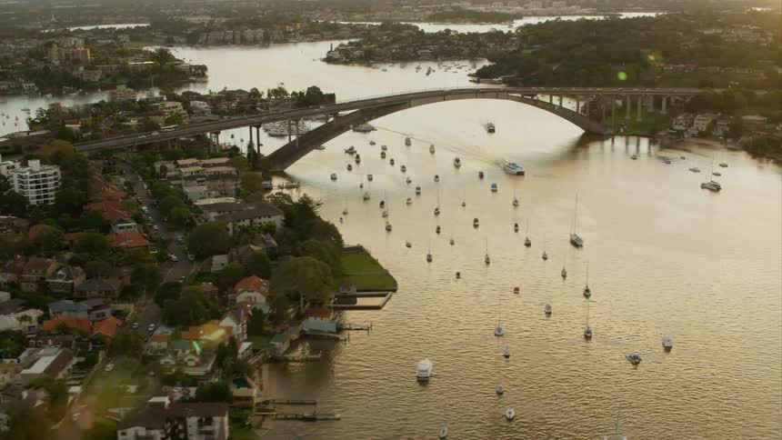 Sailboats move down a river near dense neighborhoods built on islands Sydney Harbour
