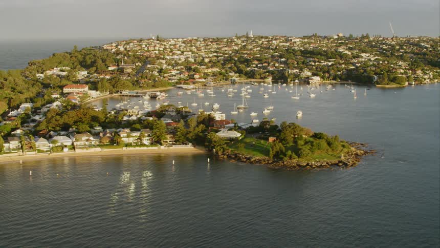 Sailboats float in a bay sitting next to a small town Sydney Harbour