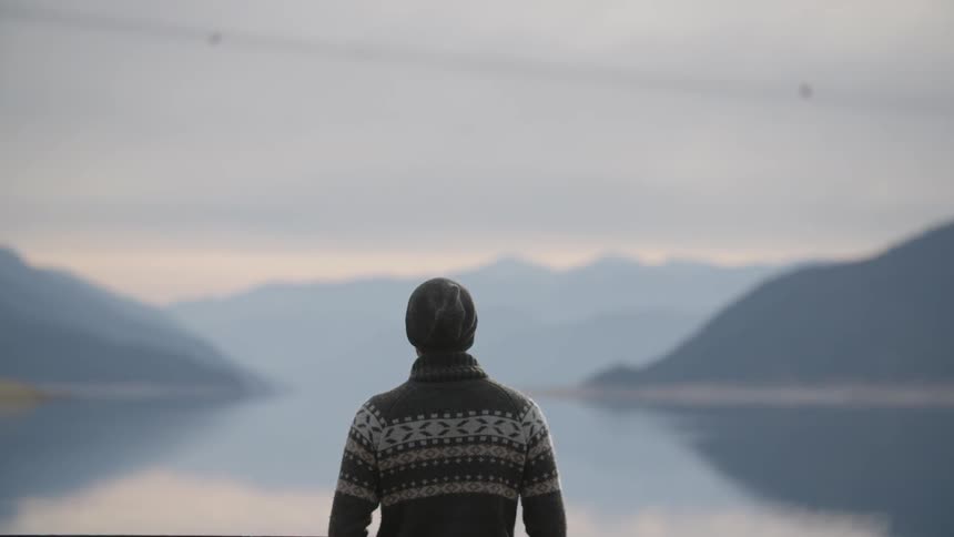 A man is standing before a large lake on a cloudy day