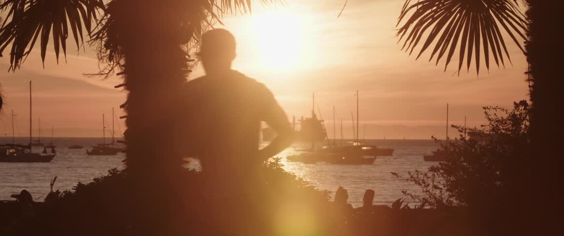 People relaxing and exercising on the shore of a bay filled with boats and ships at sunset