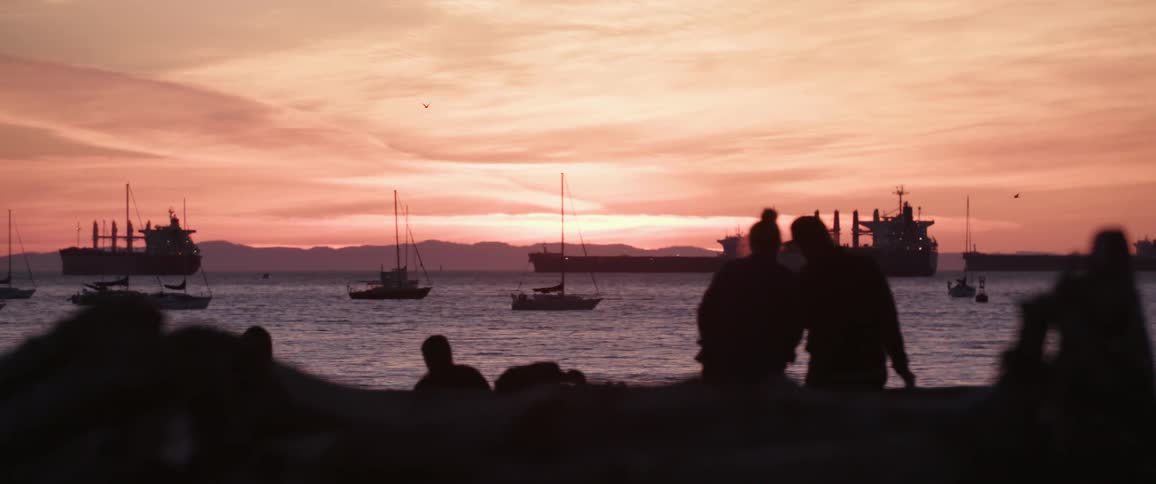 People sit and walk on a beach as boats float off the coast in the ocean