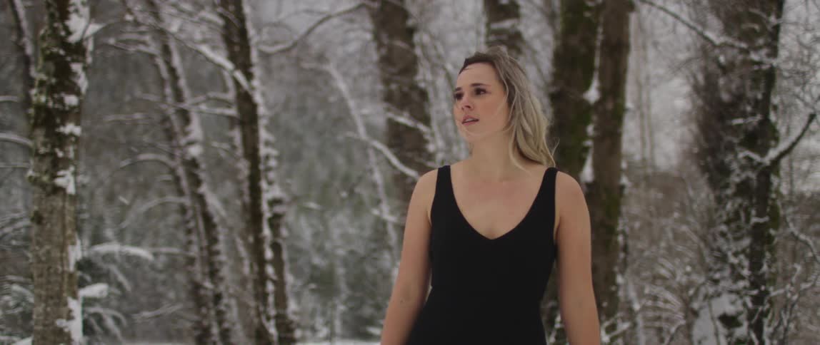 Woman in a sleeveless top walks in the snowy forest as snow falls
