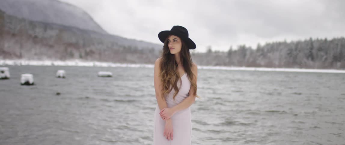 A woman poses by the lake with a hat on