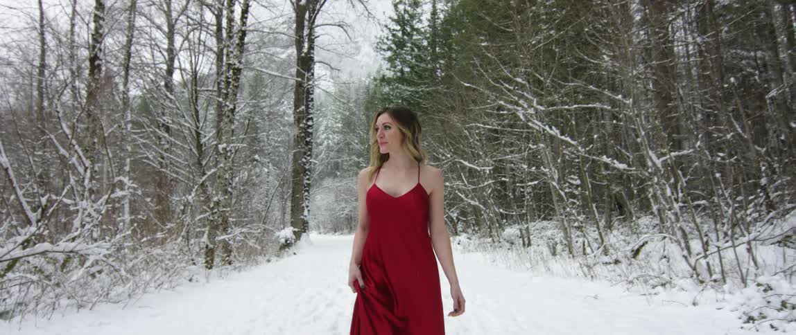 Woman wearing a red dress walks in the snow covered forest