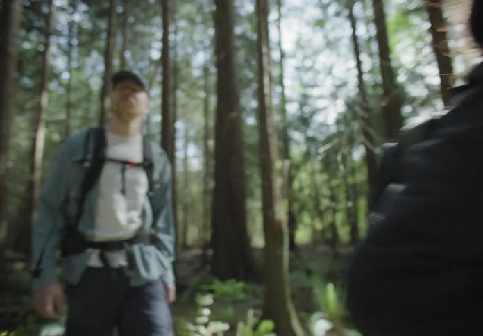 A couple hike through the woods on a sunny day each with a backpack