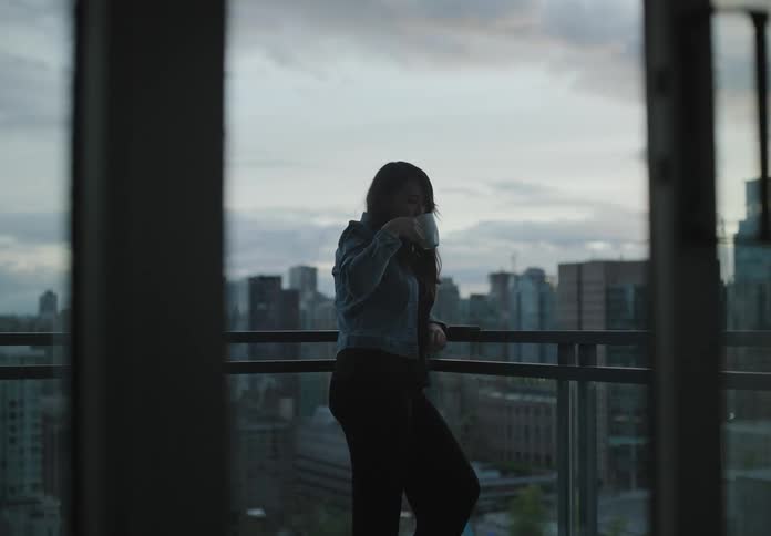 A teenager stands on her balcony drinking coffee