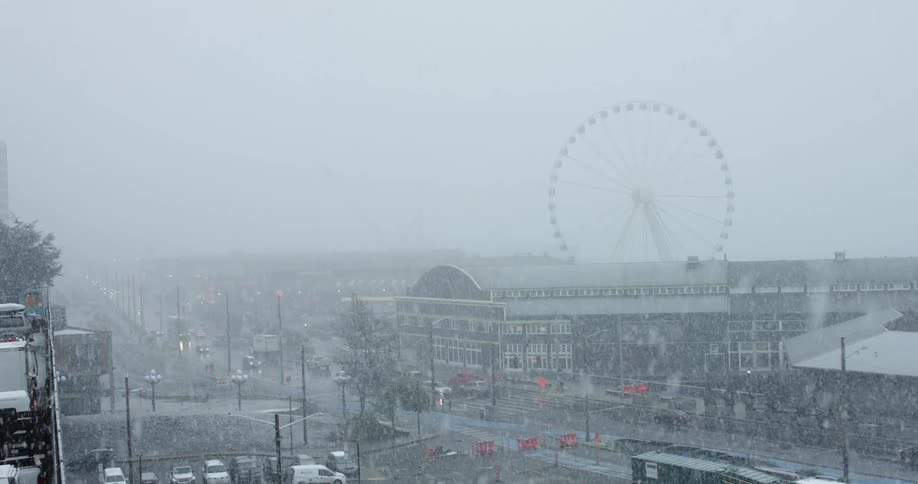 Snow falls in Seattle as people and cars go down a street