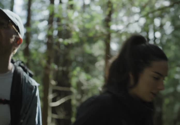 Couple wearing backpacks hike through the woods at day