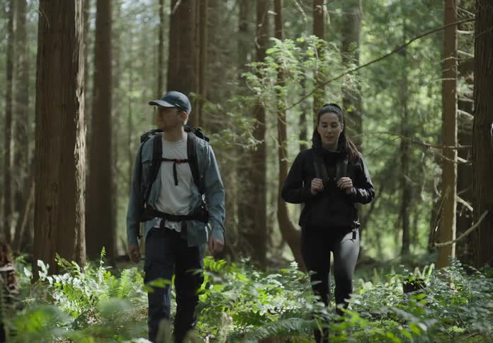 A man and woman are hiking through a forest area