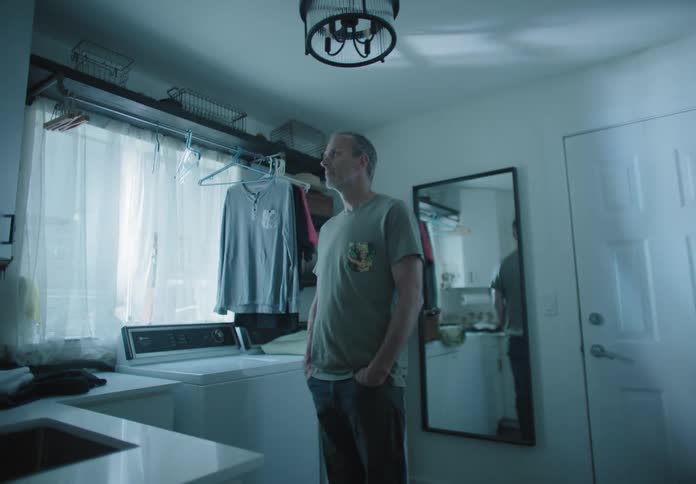 A white man stands in a washing room and looks at a light shining in the window