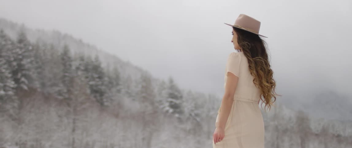 A woman poses in a dress near a forest with a light dusting of snow