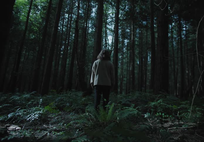 A white woman stands in the middle of a forest