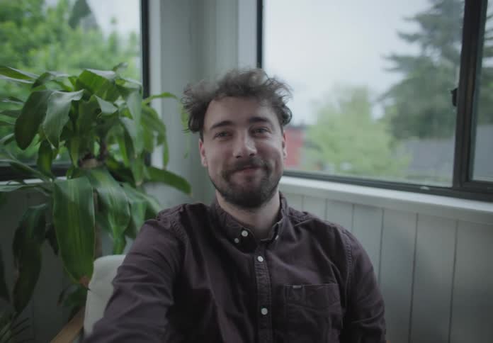 Bearded man records himself sitting on living room near windows