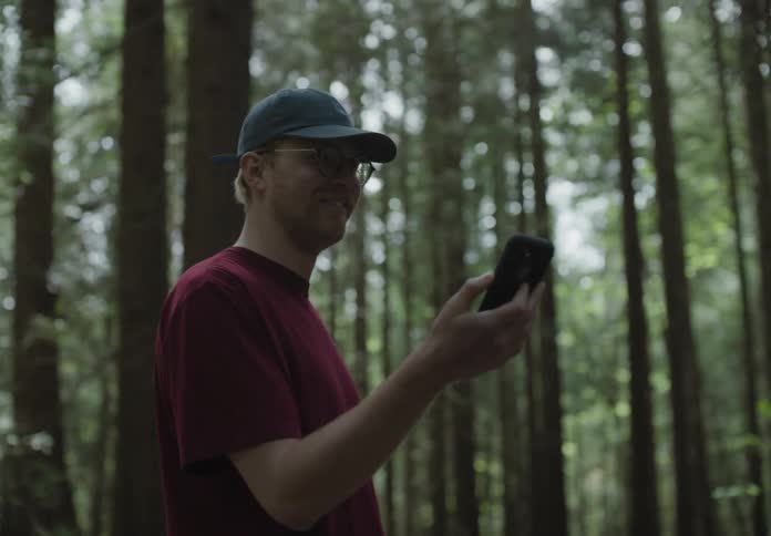 A man running through a forest before stopping to recording the surroundings with his smartphone