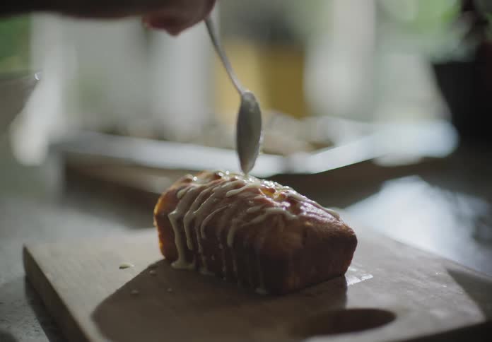 Person dripping glaze onto loaf of dessert bread from a spoon