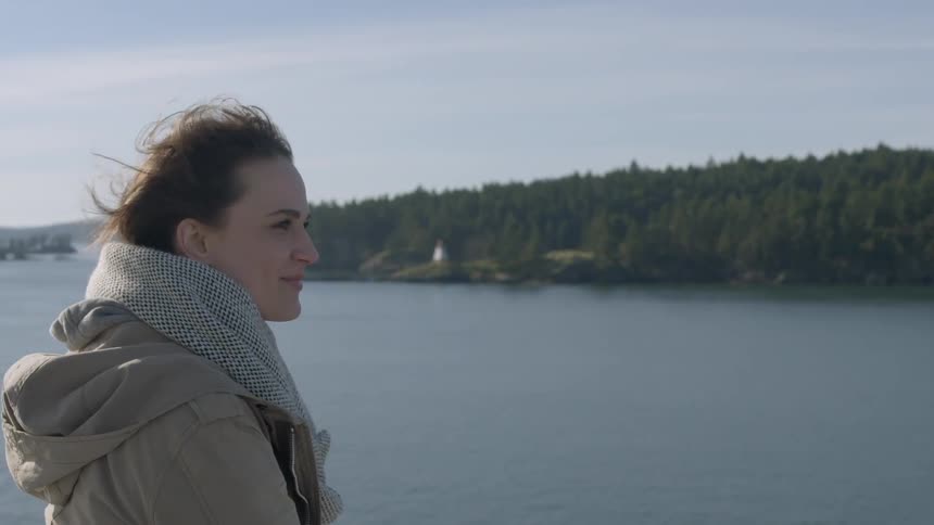 A woman is standing by a lake smiling