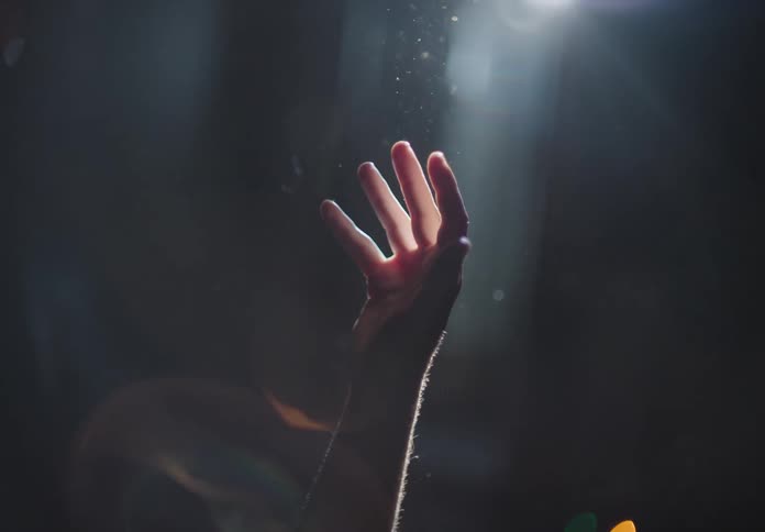 A male in the spotlight opens his hand that is raised in the air
