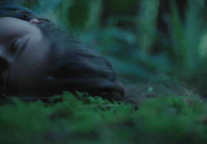 A white teenager lies on a forest floor and turns her head to the side