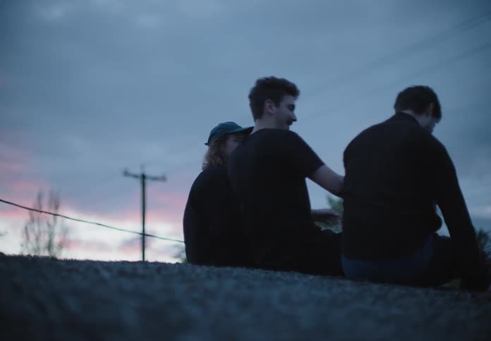 Friends sitting on a curb greet each other at sunset