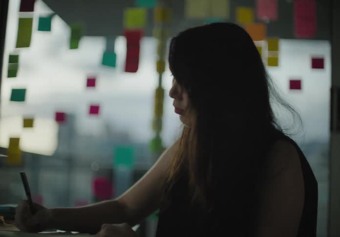 Woman sitting at the desk looks at the sticky notes and writes on the notebook