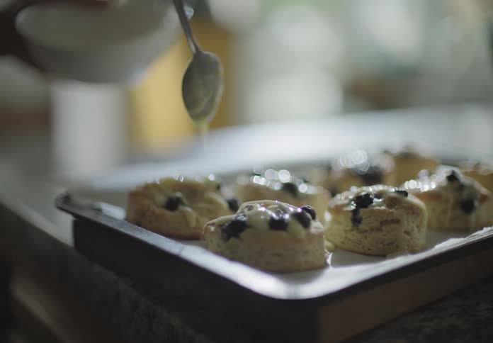 A white woman drizzles icing over a tray of biscuits