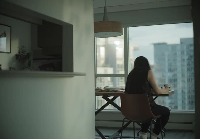 A woman takes a cup of coffee to her table and sits down as she takes a drink and then starts facetiming someone on her phone