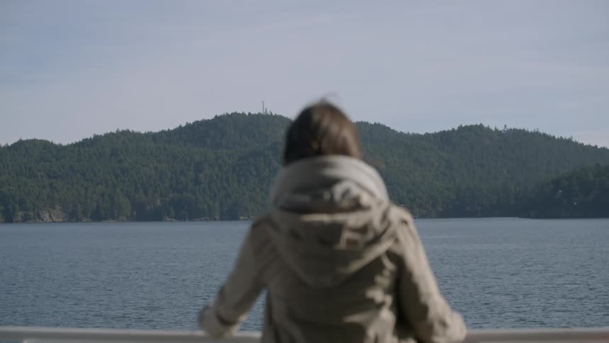 Woman standing at railing looking at water and forested land
