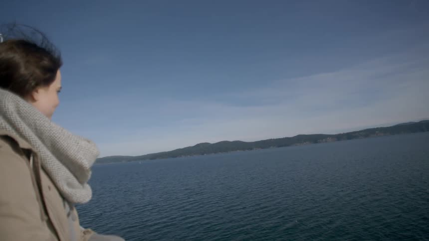 A woman is standing on a boat watching the water on a windy day