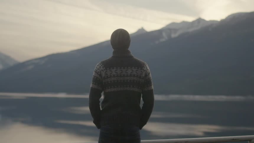 A man gazing across a mountain lake on a cold and cloudy day