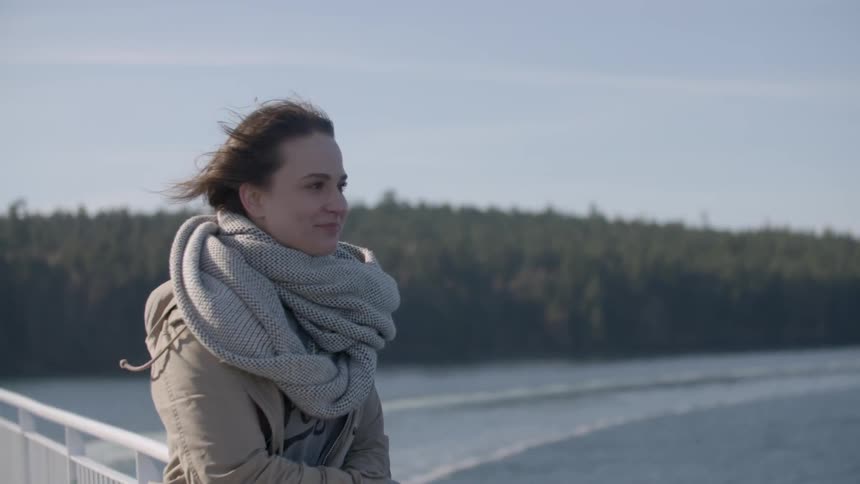 A woman in a scarf stands on a bridge on a windy day