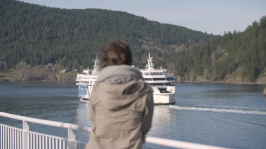 A woman in a jacket watches a boat crossing a river