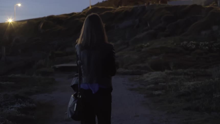 A woman is walking along a trail towards a hill at sunset
