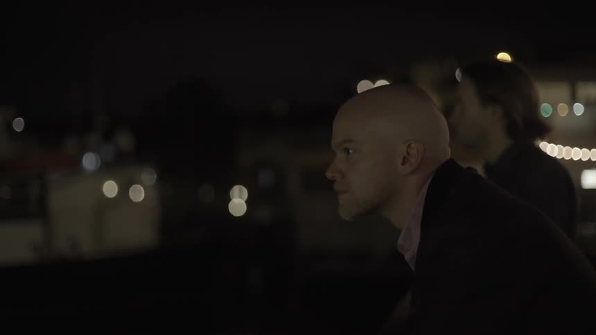 Two men standing in city at night with moody reflective urban vibe.
