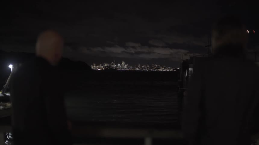 People are standing by the water at night with a city in the distance