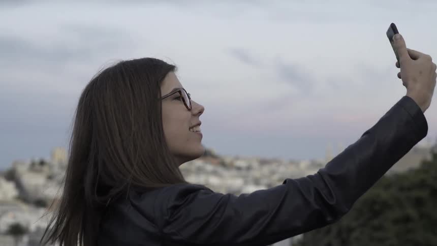 A woman raises her phone and dials on it before waving