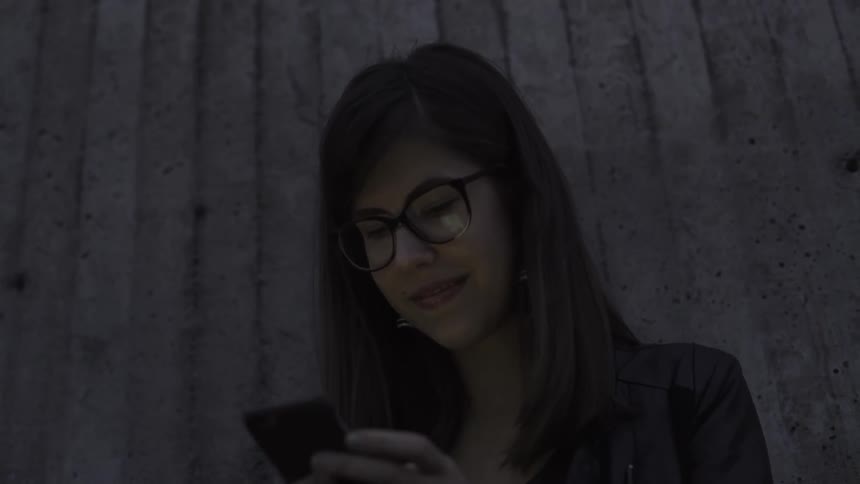 A young woman smiling as she scrolls through her phone