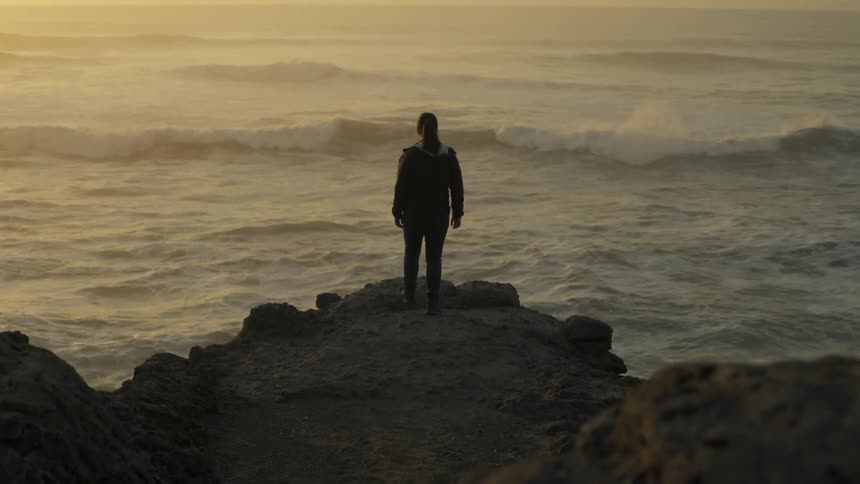 A person walks to the end of a rock overlooking the ocean