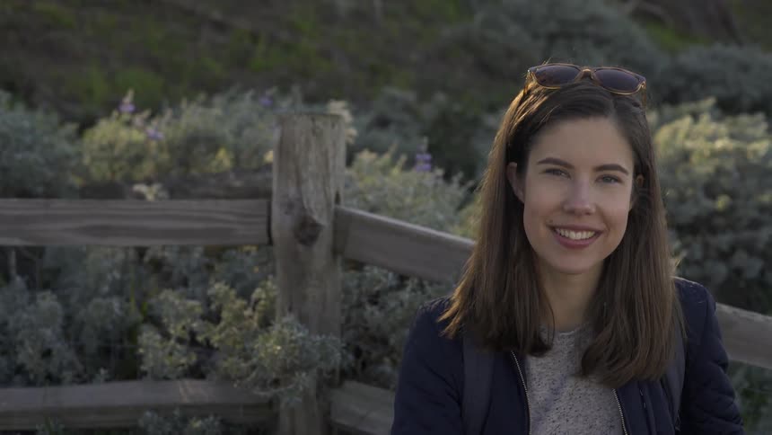 A woman stands smiling in front of a wood fence