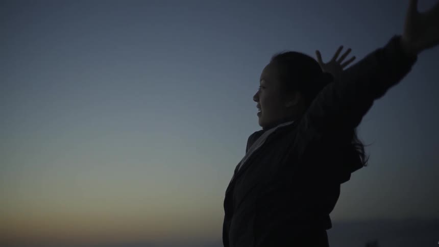 A woman is standing outside at sunset raising her arms